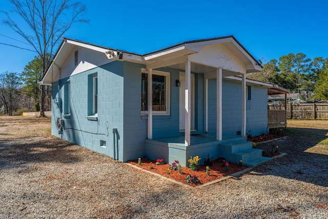 view of front of house featuring a porch, crawl space, concrete block siding, and fence