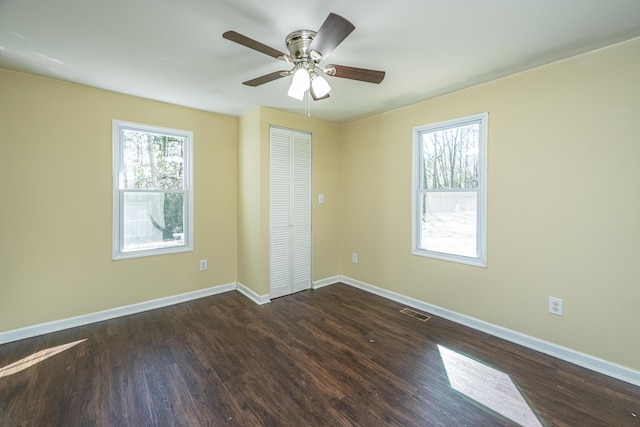 unfurnished bedroom with dark wood-type flooring, multiple windows, visible vents, and baseboards