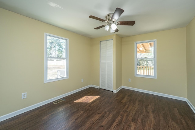 unfurnished bedroom featuring dark wood-style flooring, a closet, visible vents, a ceiling fan, and baseboards