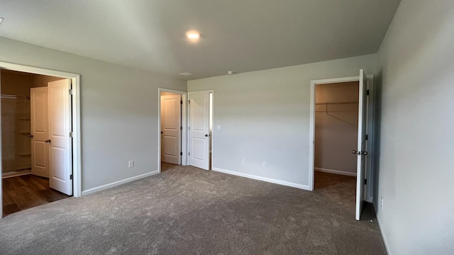 unfurnished bedroom with dark carpet, a spacious closet, and a closet