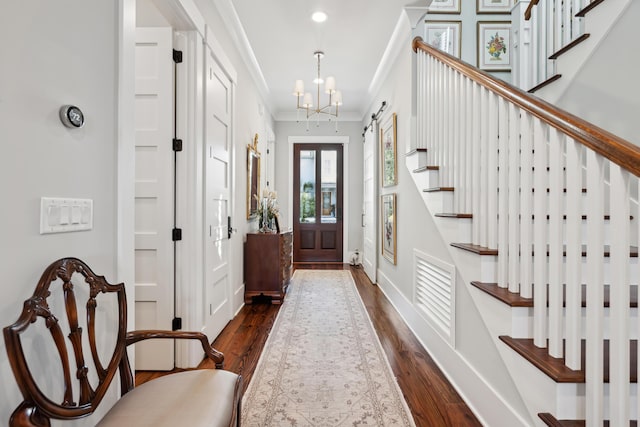 foyer entrance featuring visible vents, ornamental molding, dark wood-style flooring, stairs, and a notable chandelier