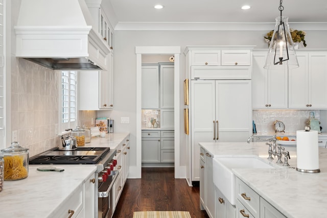 kitchen with light stone counters, custom range hood, high end stainless steel range oven, hanging light fixtures, and white cabinetry