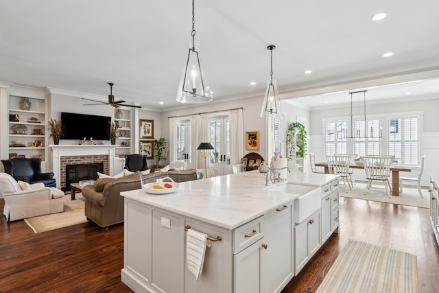 kitchen featuring open floor plan, decorative light fixtures, a center island with sink, and light stone countertops