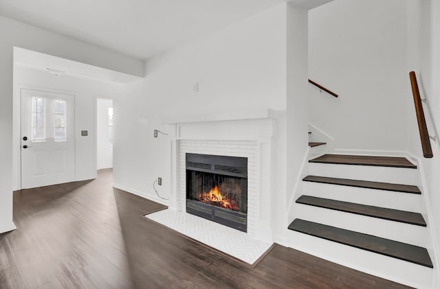 unfurnished living room featuring a brick fireplace and dark wood-type flooring