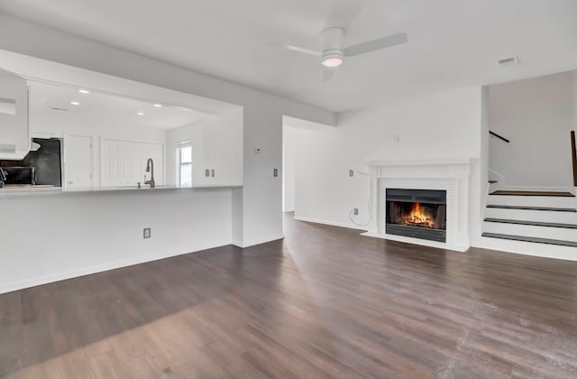 unfurnished living room with ceiling fan, dark hardwood / wood-style flooring, sink, and a brick fireplace