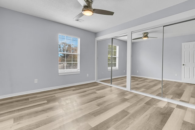 unfurnished bedroom with ceiling fan, multiple closets, a textured ceiling, and light hardwood / wood-style flooring