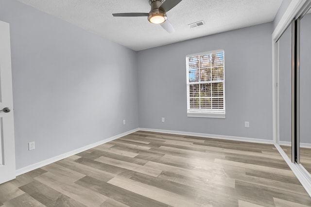 unfurnished bedroom with ceiling fan, a closet, light hardwood / wood-style floors, and a textured ceiling