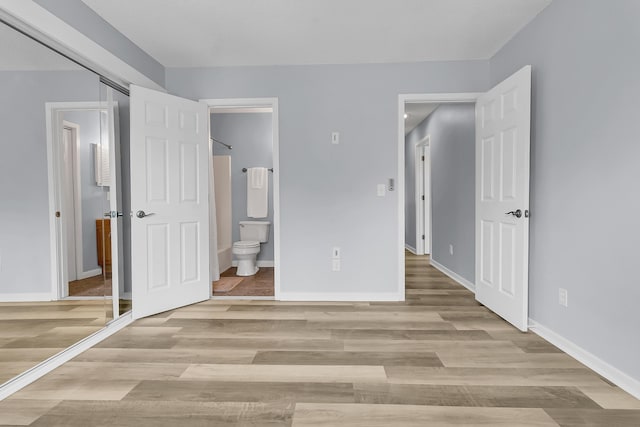 unfurnished bedroom featuring ensuite bath and light wood-type flooring