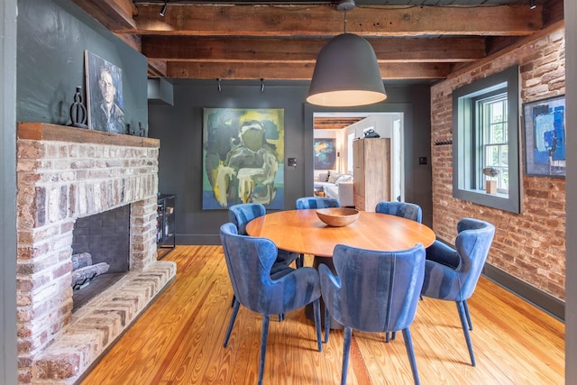dining room featuring beam ceiling, wood finished floors, baseboards, brick wall, and a fireplace