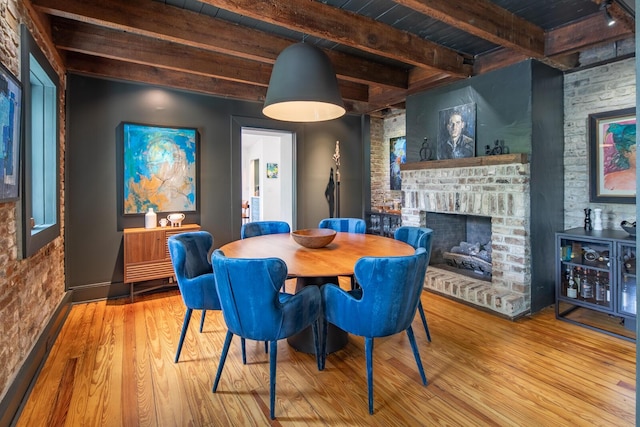 dining area featuring beam ceiling, wood finished floors, wood ceiling, a brick fireplace, and baseboards