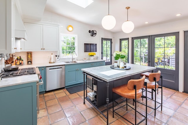 kitchen with appliances with stainless steel finishes, a sink, vaulted ceiling, blue cabinets, and decorative backsplash