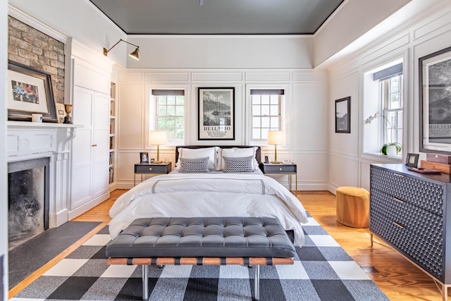 bedroom with light wood-style floors, a fireplace with flush hearth, a decorative wall, and crown molding