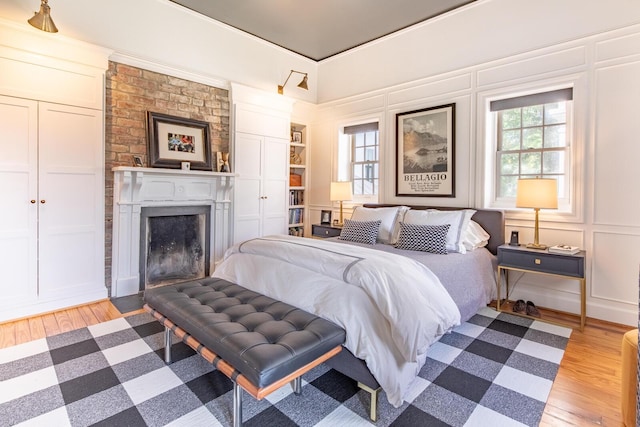 bedroom featuring light wood-style floors, a decorative wall, multiple windows, and a fireplace