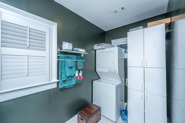 clothes washing area featuring cabinets and stacked washer and dryer