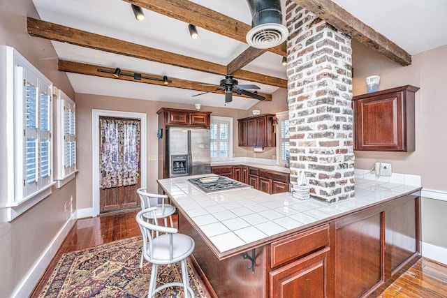 kitchen featuring dark wood-type flooring, appliances with stainless steel finishes, a kitchen bar, tile countertops, and kitchen peninsula