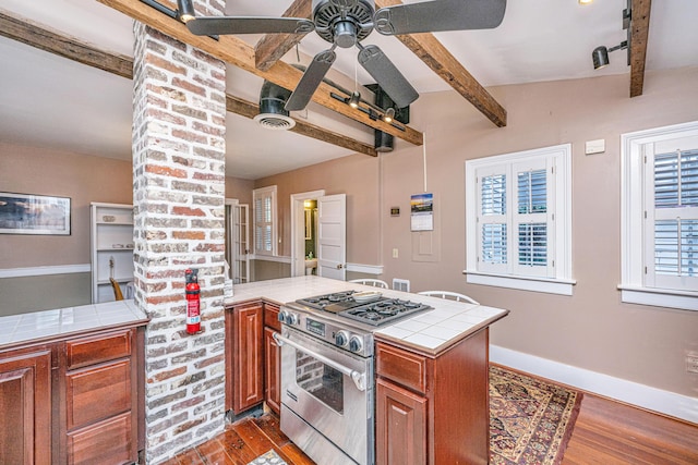 kitchen featuring dark wood-type flooring, tile countertops, gas stove, and ceiling fan