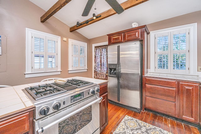 kitchen with vaulted ceiling with beams, hardwood / wood-style flooring, tile counters, ceiling fan, and stainless steel appliances