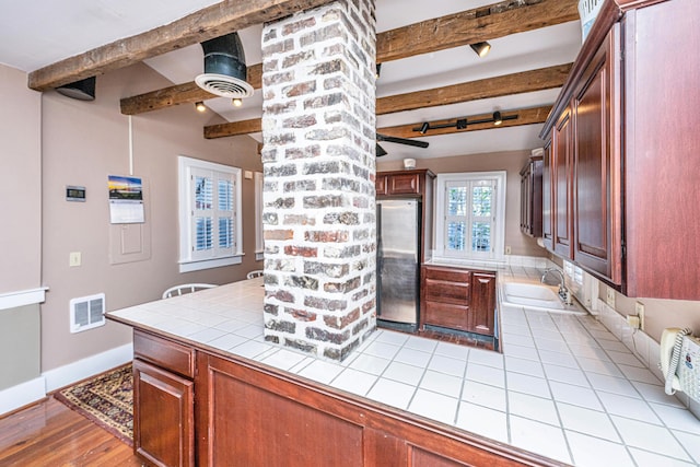 kitchen featuring beam ceiling, sink, tile counters, and stainless steel refrigerator