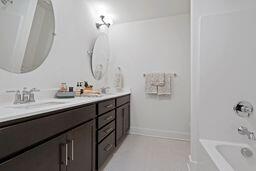 bathroom with a sink, baseboards, tub / shower combination, tile patterned floors, and double vanity