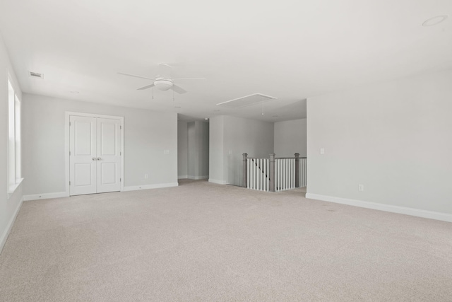 empty room featuring light carpet, attic access, baseboards, and a ceiling fan