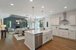 kitchen featuring light countertops, white cabinets, wall chimney range hood, and stainless steel dishwasher