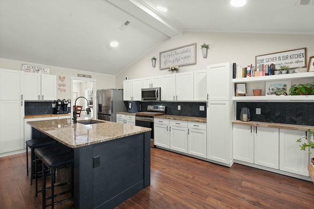 kitchen featuring sink, white cabinetry, stainless steel appliances, light stone countertops, and a center island with sink