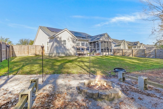 back of house featuring a lawn, a sunroom, solar panels, and an outdoor fire pit