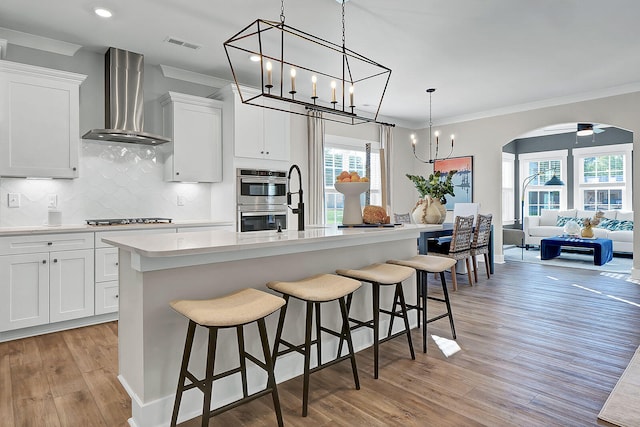 kitchen featuring arched walkways, double oven, ornamental molding, gas cooktop, and wall chimney exhaust hood