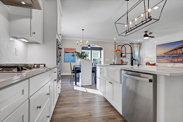 kitchen featuring arched walkways, tasteful backsplash, appliances with stainless steel finishes, ventilation hood, and wood finished floors