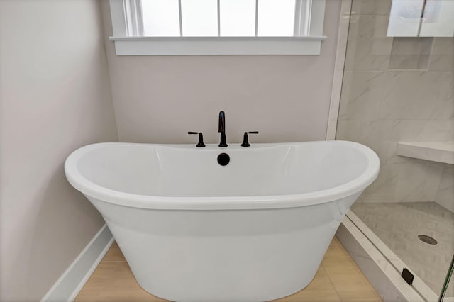 full bath featuring wood finished floors, tiled shower, a freestanding tub, and baseboards