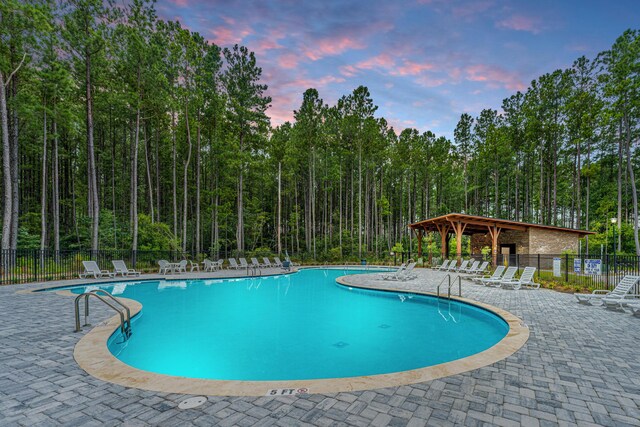 pool at dusk with a patio area, fence, and a community pool