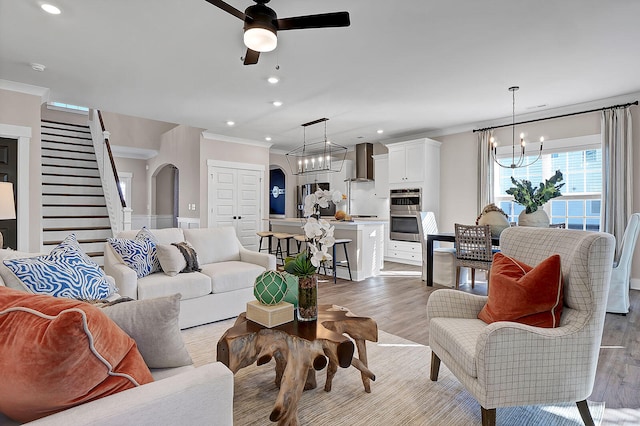 living room featuring light wood finished floors, arched walkways, ornamental molding, ceiling fan with notable chandelier, and recessed lighting