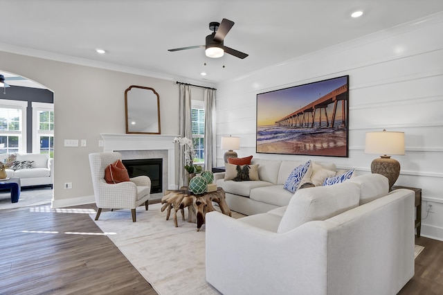 living area featuring baseboards, a ceiling fan, a premium fireplace, wood finished floors, and crown molding