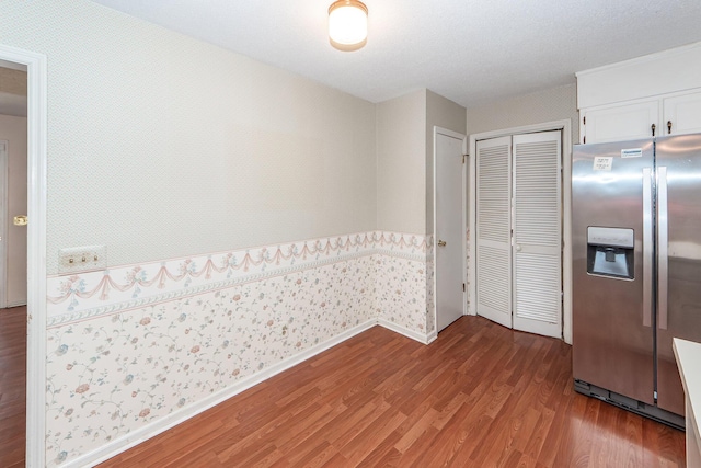 kitchen featuring stainless steel refrigerator with ice dispenser, white cabinets, wood finished floors, baseboards, and wallpapered walls