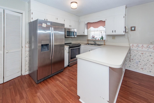 kitchen featuring a peninsula, appliances with stainless steel finishes, a sink, and wallpapered walls