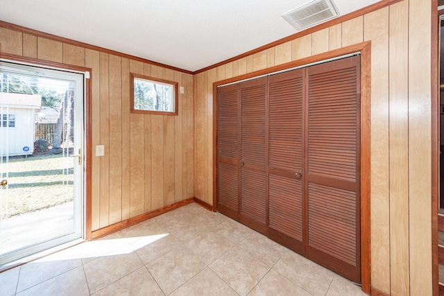 doorway featuring crown molding, light tile patterned floors, visible vents, wooden walls, and baseboards