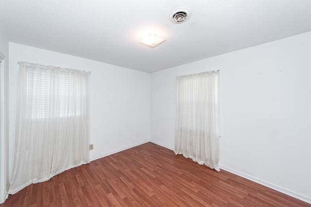 empty room featuring baseboards, a textured ceiling, visible vents, and wood finished floors