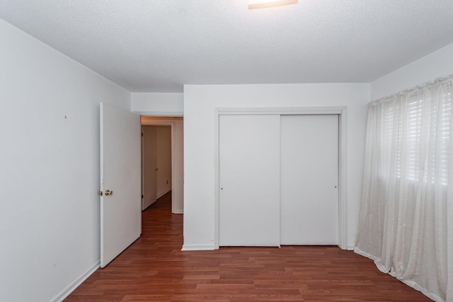 unfurnished bedroom with a closet, a textured ceiling, baseboards, and wood finished floors