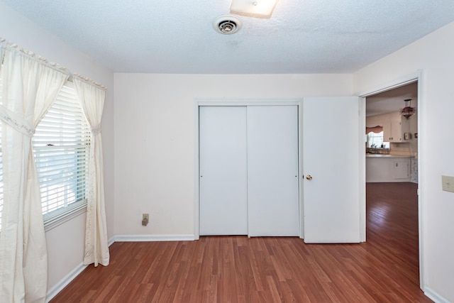 unfurnished bedroom featuring a textured ceiling, wood finished floors, visible vents, baseboards, and a closet