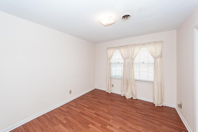 unfurnished room featuring visible vents, a textured ceiling, baseboards, and wood finished floors