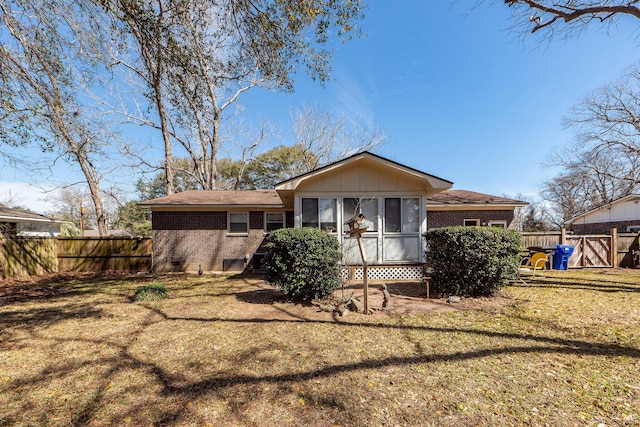 rear view of property with board and batten siding, fence, a lawn, and brick siding