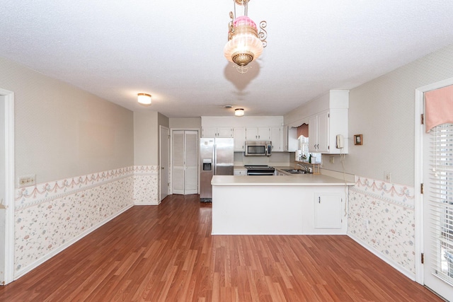 kitchen with stainless steel appliances, wainscoting, wood finished floors, a peninsula, and wallpapered walls