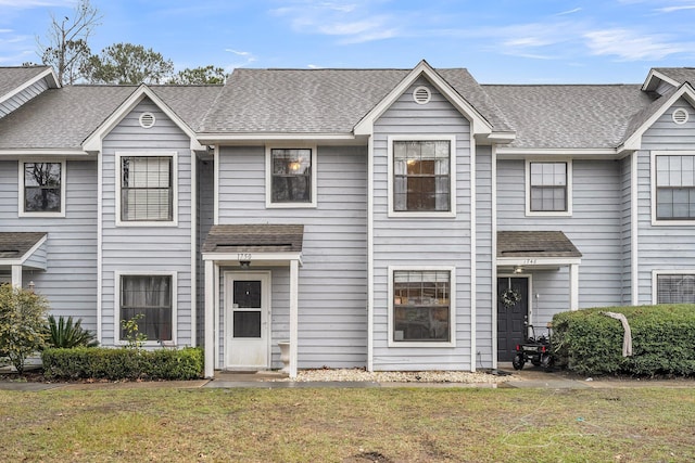 view of property with a shingled roof and a front yard