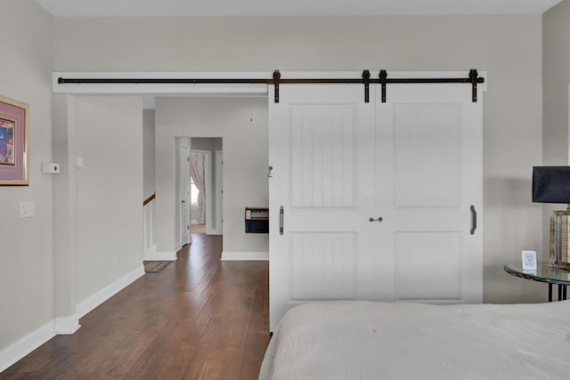 bedroom featuring dark wood-style flooring, baseboards, and a barn door