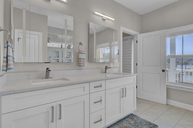 bathroom featuring marble finish floor, double vanity, a sink, and baseboards