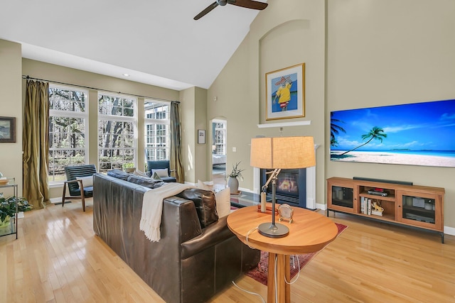 living room with arched walkways, baseboards, a tile fireplace, light wood-style flooring, and high vaulted ceiling