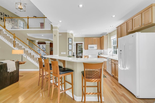 kitchen with white appliances, ornamental molding, a breakfast bar, light countertops, and light wood-type flooring