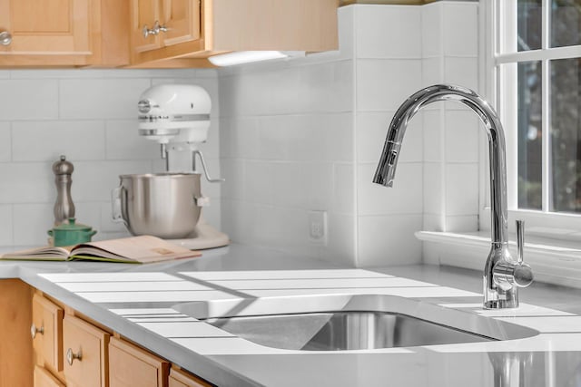 interior details featuring a sink, light brown cabinets, light countertops, and backsplash