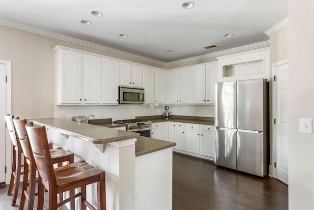 kitchen featuring white cabinets, a kitchen breakfast bar, kitchen peninsula, decorative backsplash, and appliances with stainless steel finishes