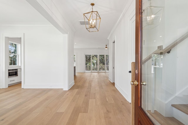 corridor featuring crown molding, light wood-style flooring, an inviting chandelier, a healthy amount of sunlight, and stairs